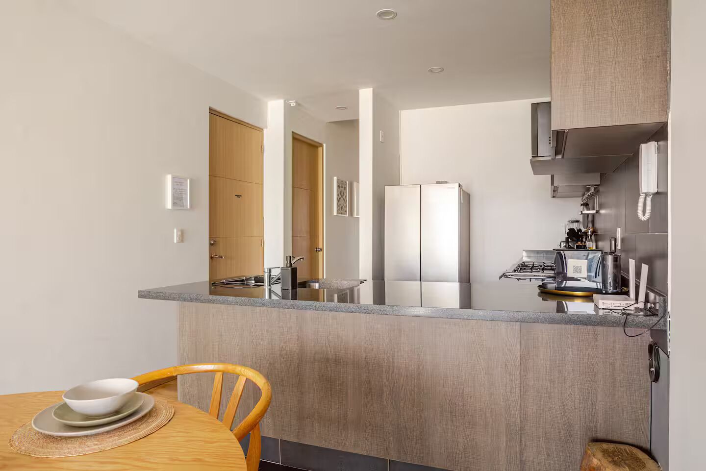 Una cocina compacta con refrigerador integrado, estufa y microondas. Cuenta con una mesa de comedor, una silla y un tapete pequeño.