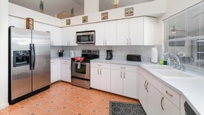 A modern kitchen with white cabinets, stainless steel appliances, and a tiled floor. - Sunshine Vibes • Pool, Hot Tub & Kayaks (Cape Coral)