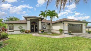 A two-story house with a garage, a front porch, and a well-maintained lawn. - Sunshine Vibes • Pool, Hot Tub & Kayaks (Cape Coral)