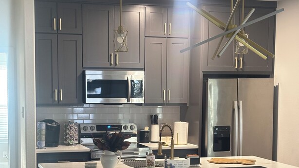 A modern kitchen with grey cabinets, stainless steel appliances, and a central island with stools. -  Modern 4BR/2.5BA Townhouse in the Heart of Fort Worth (Fort Worth)