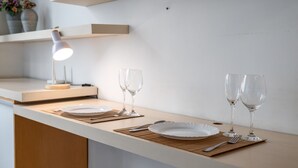 A clean, modern kitchen with white cabinetry, a wooden countertop, and a minimalist design. There are two wine glasses and a plate on the counter, along with a small lamp providing light. - 1 Minuto Da Praia De Copacabana | A923 (Rio de Janeiro)