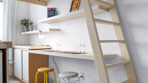 A room with a slanted ceiling, a desk with a chair, a ladder, and a shelf with a picture frame. - 1 Minuto Da Praia De Copacabana | A923 (Rio de Janeiro)