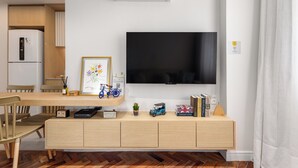 A modern living room with a flat-screen TV, wooden furniture, a small bookshelf, and a herringbone-patterned floor. - Luxo Na Barra Da Tijuca Próximo Ao Parque Olímpico | Av806 (Rio de Janeiro)