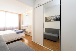 Een moderne hotelkamer met een bed, een grijze bank, een klein tafeltje en een inloopkast met schuifdeuren.