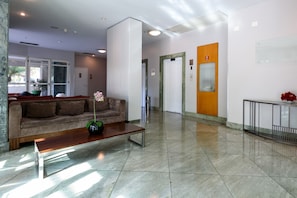A lobby with a sofa, a coffee table, a potted plant, and a reception desk. - Suíte Piscina E Academia | Bpremium T1 1208.4 (Rio de Janeiro)