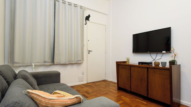 A living room with a grey sofa, a wooden cabinet, a flat-screen TV, and a door with a cat silhouette. - Sossego Em Copa | Vista Arborizada | Br1009 (Rio de Janeiro)