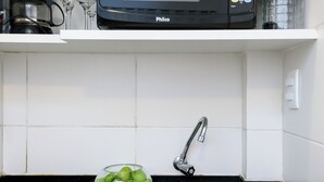 A kitchen with a black microwave, a sink, a bowl of green apples, and a coffee maker. - Sossego Em Copa | Vista Arborizada | Br1009 (Rio de Janeiro)