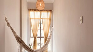 A hammock hanging in a room with a large window, a hanging light fixture, and a small ottoman. - 6 Minutos Da Praia De Copacabana | Br1033 (Rio de Janeiro)