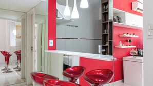 A modern kitchen with red and white cabinetry, a white countertop, and stainless steel appliances. There are three red bar stools and a hanging light fixture above the counter. - Perfeito Em Copacabana |Quarto Confortável| Br401 (Rio de Janeiro)