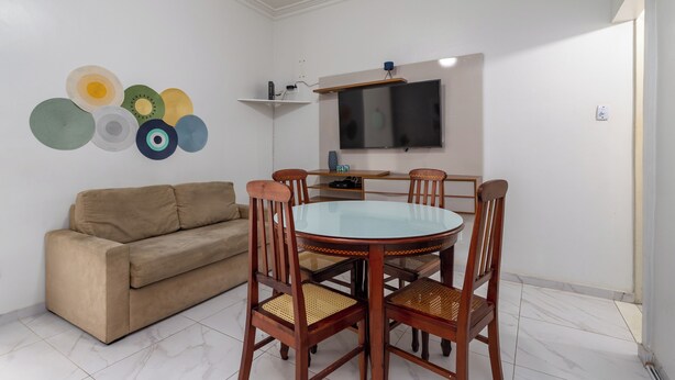 A dining area with a round table, four wooden chairs, a beige sofa, and a wall-mounted TV. - Estilo Em Copacabana | Próximo A Praia | Br403 (Rio de Janeiro)