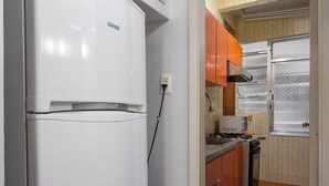 A compact kitchen with a white refrigerator, orange cabinets, and a tiled floor. - Estilo Em Copacabana | Próximo A Praia | Br403 (Rio de Janeiro)