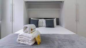 A neatly made bed with a gray blanket, a stack of white towels, and a small bag of toiletries. - Conforto A 6Min Da Praia De Copacabana | Br801 (Rio de Janeiro)