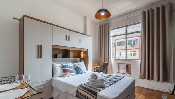 A hotel room with a bed, a desk, a chair, a table with glasses, and a window with curtains. - 5Min Da Praia De Copacabana | Br902 (Rio de Janeiro)