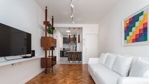 A modern living room with a flat-screen TV, wooden flooring, a white sofa, and a colorful abstract painting. - 5 Minutos Da Praia E Vista Para O Cristo | Br904 (Rio de Janeiro)
