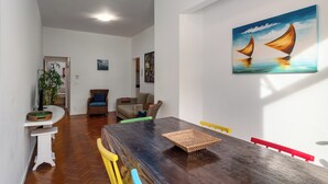A dining area with a wooden table, chairs, and a painting of sailboats. - Aconchego Em Copa | Ideal P/ Família | Brx1005 (Rio de Janeiro)