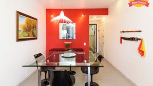 A dining area with a glass table and chairs, a red accent wall, a hanging light fixture, and a framed painting. - Excelente Em Ipanema |Ambiente Familiar| Bt101 (Rio de Janeiro)