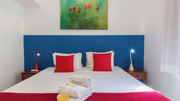 Ένα στρωμένο κρεβάτι με προσεγμένο τρόπο, με κόκκινα και λευκά μαξιλάρια, ένα μπλε προσκέφαλο και έναν πίνακα με κόκκινες τουλίπες τοποθετημένο ακριβώς από πάνω.