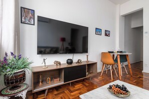 Una sala de estar con televisor de pantalla plana, mueble de madera para entretenimiento y comedor con mesa y sillas.