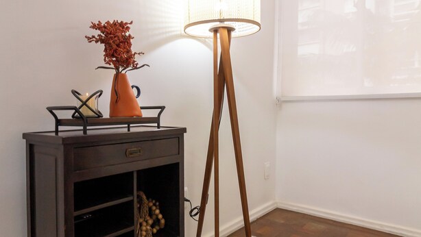 Una habitación con una consola de madera oscura, una lámpara de pie y un ventanal con persianas.