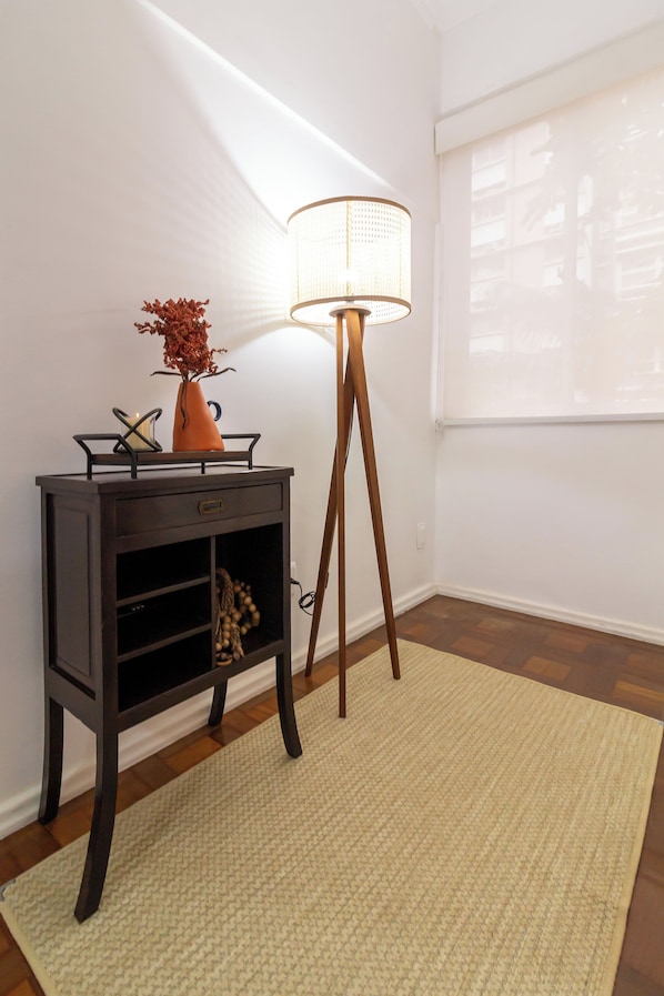Une pièce avec une console en bois foncé, un lampadaire et une fenêtre équipée de stores.