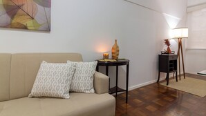 Una sala de estar con un sofá color beige, almohadones estampados, una mesita con una vela y una lámpara de pie.