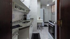 Una cocina compacta con encimera de granito, un lavamanos, una estufa y un armario blanco.