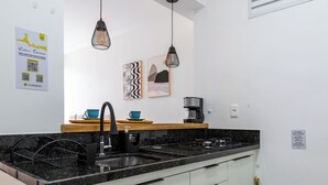 A modern kitchen with a black countertop, white cabinets, a coffee machine, and pendant lights. - 10 Minutos Da Praia Do Flamengo Ao Lado Do Metrô | Ct404 (Rio de Janeiro)