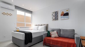 A modern bedroom with a bed, a grey sofa, and two wall-mounted artworks. - 10 Minutos Da Praia Do Flamengo Ao Lado Do Metrô | Ct404 (Rio de Janeiro)