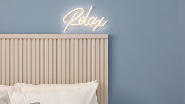 Une chambre à coucher avec un lit, des oreillers, une table de chevet et un néon mural.