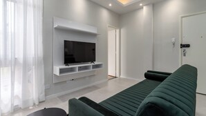 Un salon moderne avec un téléviseur à écran plat fixé à un mur blanc, un canapé vert et une petite table.