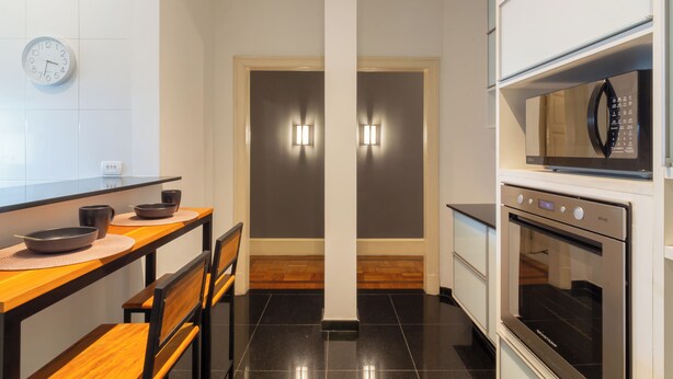 A modern kitchen with a wooden table, chairs, a microwave, and an oven. - Espaço E Conforto Em Copacabana | D405 (Rio de Janeiro)