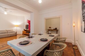 Un coin repas avec une longue table dressée pour quatre personnes, entourée de chaises en osier.