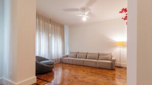 A modern living room with a wooden parquet floor, a grey sofa, a grey armchair, and a ceiling fan. - Espaço E Conforto Em Copacabana | D405 (Rio de Janeiro)