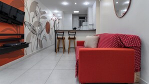 A modern living room with a red sofa, a TV mounted on the wall, and a kitchen area in the background. - 3 Minutos Da Praia De Copacabana | Df219 (Rio de Janeiro)
