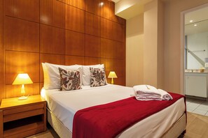 A hotel room with a wooden headboard, a bed with white bedding and a red throw, two bedside lamps, and a neatly made bed with towels. - 2 Minutos Da Praia De Copacabana | Df408 (Rio de Janeiro)