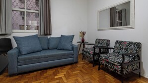 A living room with a grey sofa, patterned armchairs, a small table with a vase, and a large mirror on the wall. - 6 Minutos Da Praia De Copacabana | El108 (Rio de Janeiro)