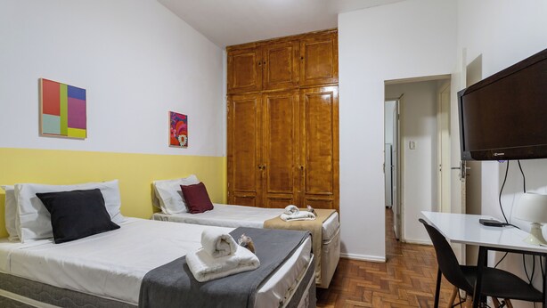 A hotel room with two beds, a wooden wardrobe, a television, and a desk with a chair. - 6 Minutos Da Praia De Copacabana | El108 (Rio de Janeiro)