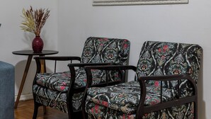 A room with a wooden floor, two patterned armchairs, a small round table with a vase, and a large mirror on the wall. - 6 Minutos Da Praia De Copacabana | El108 (Rio de Janeiro)