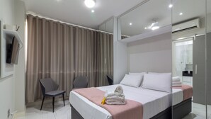 A modern hotel room with a large bed, a desk with a chair, a mirror, and a shower area. - Adorável A Poucos Minutos Do Pão De Açúcar | F709 (Rio de Janeiro)
