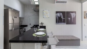 A modern kitchen with a black countertop, stainless steel appliances, and a seating area with a bench. - Adorável A Poucos Minutos Do Pão De Açúcar | F709 (Rio de Janeiro)