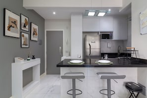A modern kitchen with a central island, bar stools, a microwave, and a refrigerator.