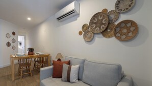 Ein Wohnzimmer mit grauem Sofa, einem Holzesstisch mit Stühlen und einer Wand-Klimaanlage.