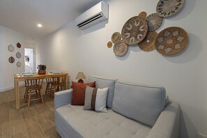 Ein Wohnzimmer mit grauem Sofa, einem Holzesstisch mit Stühlen und einer Wand-Klimaanlage.