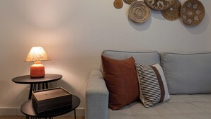 Ein Wohnzimmer mit einem grauen Sofa, einem runden Tisch mit einer Lampe und einer kleinen Holzkiste.