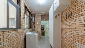 A narrow kitchen with a brick wall, a washing machine, and a refrigerator. - Vista Para O Mar 2 Minutos Da Praia | Fms502 (Rio de Janeiro)