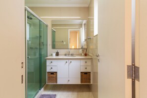 A modern bathroom with a glass shower enclosure, a large mirror, and a white vanity with two wicker baskets. - Vista Para O Mar 2 Minutos Da Praia | Fms502 (Rio de Janeiro)