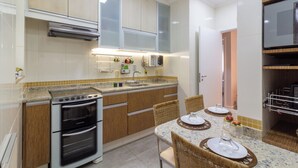 A modern kitchen with wooden cabinets, a built-in oven, and a dining area with a table set for two. - Vista Para O Mar 2 Minutos Da Praia | Fms502 (Rio de Janeiro)