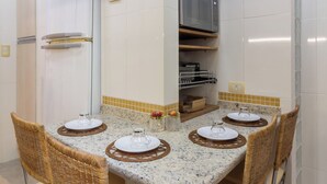 A compact kitchen with a dining table set for four, equipped with stainless steel appliances and a tiled backsplash. - Vista Para O Mar 2 Minutos Da Praia | Fms502 (Rio de Janeiro)