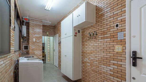 A narrow hallway with a brick wall, a white washing machine, and a white wardrobe. - Vista Para O Mar 2 Minutos Da Praia | Fms502 (Rio de Janeiro)