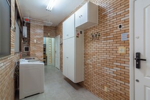 A narrow hallway with a brick wall, a white washing machine, and a white wardrobe. - Vista Para O Mar 2 Minutos Da Praia | Fms502 (Rio de Janeiro)
